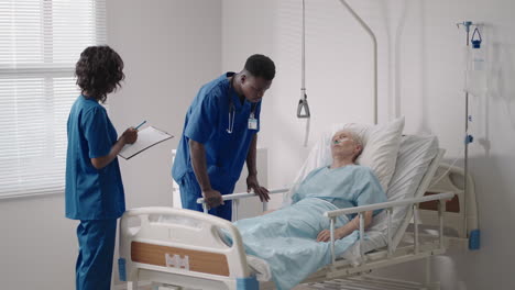 Un-Médico-Negro-Y-Una-Enfermera-Entrevistan-A-Un-Paciente-Anciano,-Un-Pensionista-En-El-Hospital-Y-Cuidan-Su-Salud
